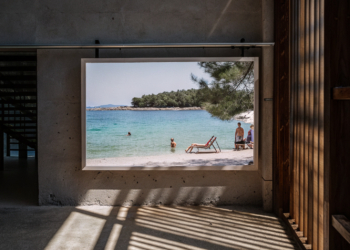A pebble beach on the Croatian coast with clear Adriatic water and light shade from pine trees