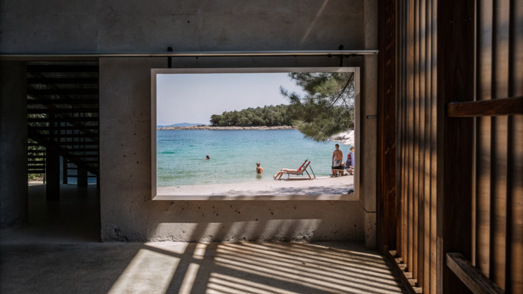 A pebble beach on the Croatian coast with clear Adriatic water and light shade from pine trees