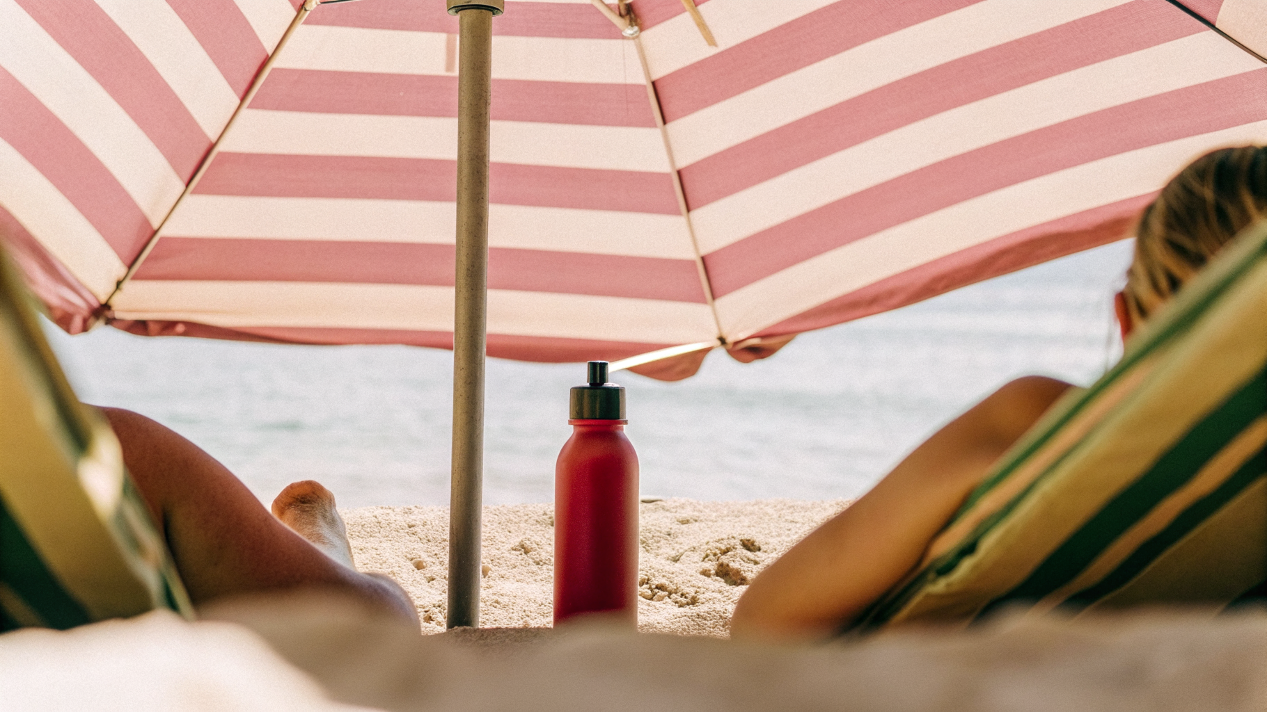A beach umbrella and water bottle providing shade on a hot Croatian beach at midday