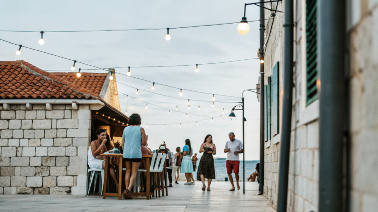 Friends enjoying drinks on an old-town bar terrace at dusk on the Croatian coast