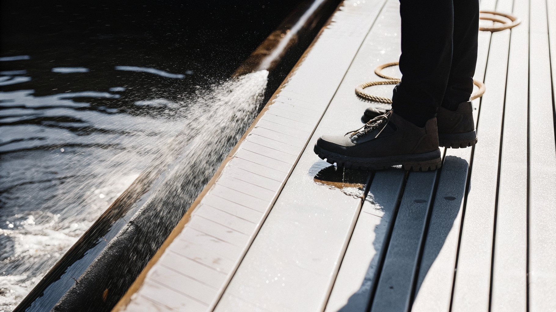 Wet slippery wooden boardwalk planks beside deep water with a hiker's shoes stepping carefully