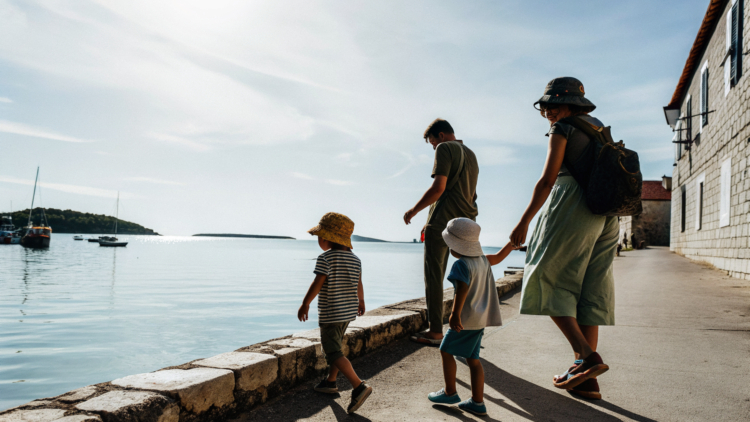 Family with young children walking a sunny Croatian seafront promenade beside calm Adriatic water